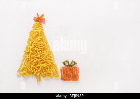 Albero di Natale alternativo di pasta secca coloso fusilli con regalo su sfondo bianco. Buon biglietto di auguri natalizio con spazio per la copia. Vista dall'alto. Cibo Foto Stock