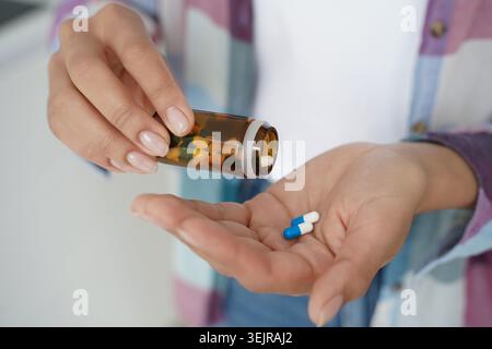 Donna che versa pillole dalla bottiglia della medicina alla mano per i farmaci quotidiani Foto Stock
