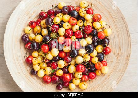 Ciliegie rosse gialle e scure servite in una ciotola di legno sul piano portapaziente dalla vista dall'alto Foto Stock