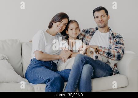 I genitori e la figlia si siedono con Jack Russell terrier sul divano bianco a casa Foto Stock