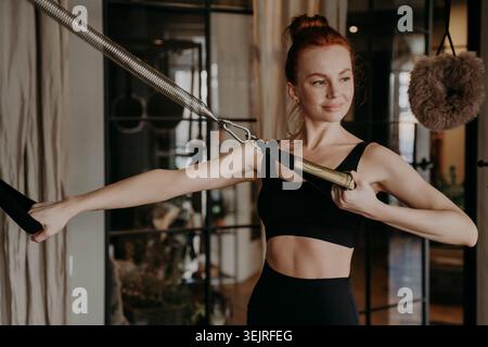 Giovane donna dai capelli rossi che si allena con i cinturini Pilates in un moderno centro fitness Foto Stock