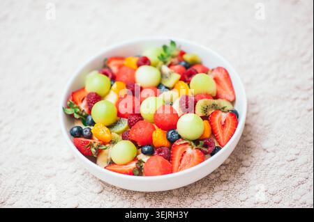 Macedonia di frutta fresca mista con frutti di bosco, melone, kiwi e fragole in una ciotola bianca Foto Stock