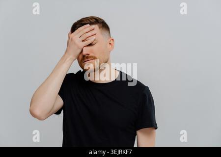 Giovane uomo che copre il viso con la mano mentre soffre di mal di testa e stress Foto Stock