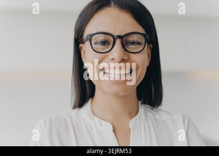 La giovane donna sorridente con occhiali neri indossa una blusa bianca per un colpo di testa professionale Foto Stock