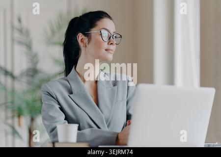 La giovane donna d'affari caucasica con gli occhiali lavora con un computer portatile in un ufficio moderno Foto Stock