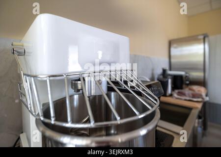Una vista ravvicinata di un mixer professionale a spirale bianco con recipiente in acciaio inox e protezione di sicurezza in metallo si trova all'interno di una cucina commerciale Foto Stock