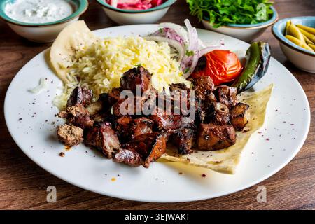 Tradizionale shashlik di fegato di agnello con riso allo zafferano, focaccia di lavanda e verdure grigliate su un piatto bianco. Baku, Azerbaigian. Foto Stock