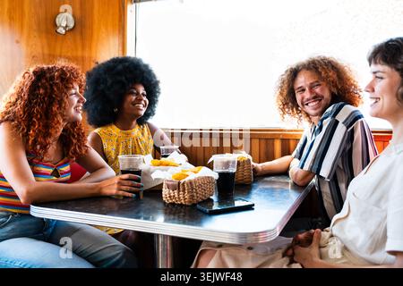 Gruppo multietnico di giovani amici felici che si uniscono al ristorante vintage hamburger House - gruppo di giovani felici e diversi che si godono spuntini e bevande Foto Stock