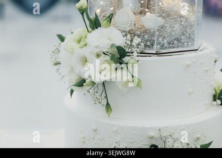 Elegante torta bianca adornata da delicati fiori Foto Stock