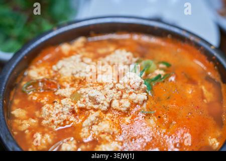 Il Sundubu-jjigae è uno speziato stufato di tofu coreano servito in una pentola calda di terracotta. Il suo tenero tofu e il saporito brodo di peperoncino rosso offrono un sapore abbondante. Foto Stock