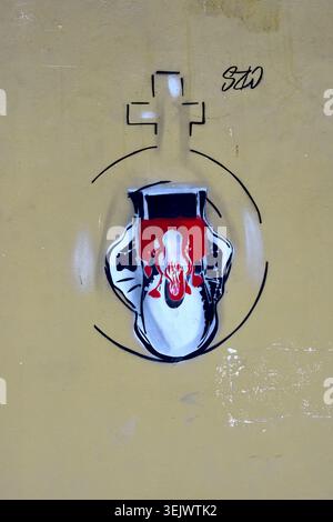 Vista verticale ravvicinata di graffiti stencil su una parete raffiguranti un simbolo stilizzato con una croce e un elemento sanguinante. Foto Stock