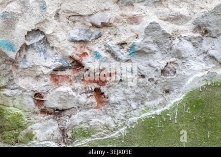 Materiali di intonaco diversi che coprono una vecchia struttura di fondo in mattoni e pietra Foto Stock