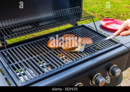 Vista ravvicinata della persona che gira le polpette di hamburger sul barbecue durante la cottura all'aperto. Svezia. Foto Stock