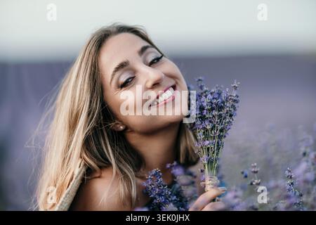 Donna campo di lavanda sorridente giovane signora che tiene un bouquet di fiori freschi in un prato viola in fiore durante il tramonto Foto Stock