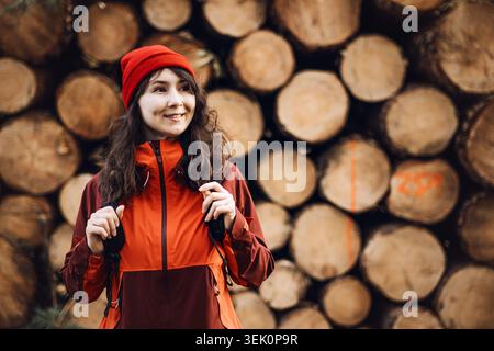 Una donna sorridente si trova di fronte a tronchi di legno impilati nell'area boschiva. Donna ispettore forestale, donna professionista industriale, ispettore ambientale Foto Stock