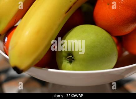 Primo piano di un cestino di frutta contenente banane, una mela verde e arance, che mostrano colori e texture vivaci con un'illuminazione soffusa e focalizzano l'attenzione sul fo Foto Stock