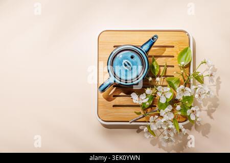 Teiera in ceramica blu con ramoscello primaverile in fiore su vassoio in legno in una composizione minimale in stile asiatico Foto Stock