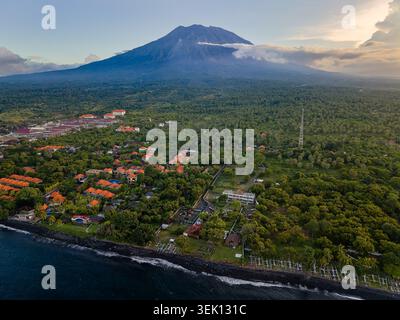 Colpo di droni del Monte Agung che incombe sul villaggio costiero di Tulamben alla luce della sera Foto Stock