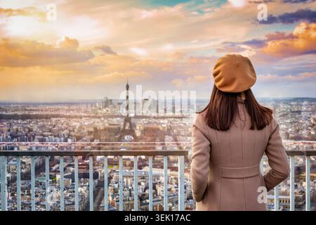 Una donna con un cappello di berretto guarda la vista panoramica del tramonto sullo skyline di Parigi, in Francia Foto Stock