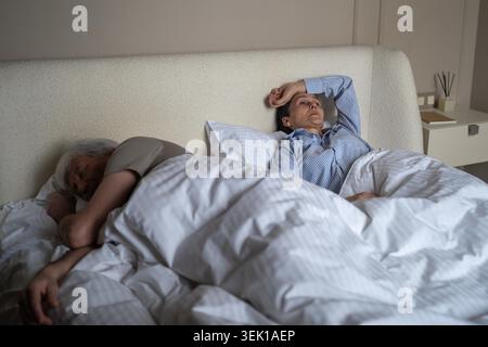 Una donna anziana frustrata che lotta con il sonno notturno a causa del marito russare fastidiosamente di notte, una donna irritata sdraiata a letto con apatia e stanchezza mentre l'uomo riposa nel sonno profondo e ruba. Foto Stock