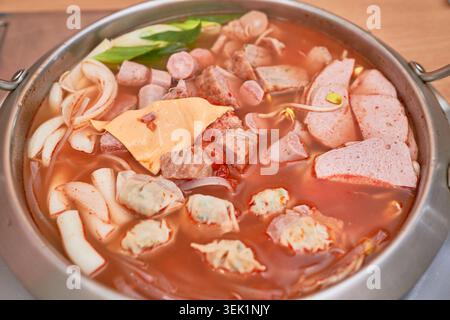 Budae-jjjigae coreana in una pentola in acciaio, con brodo piccante carico di salsicce, spamming, formaggio, gnocchi e spaghetti di ramen che bollono attivamente. Foto Stock