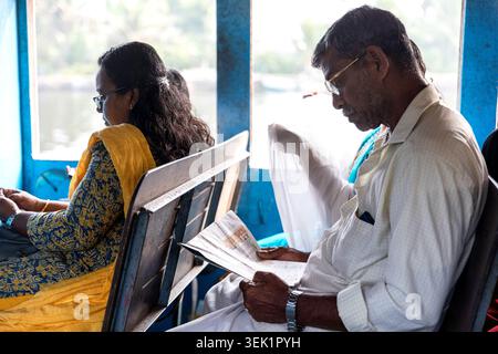 Uomo del posto con gli occhiali che legge un giornale mentre siede su un traghetto pubblico mentre va a lavorare ad alleppey, in Kerala, India, Foto Stock