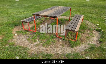 Un'immagine media ad angolo alto mostra un tavolo da picnic rustico in legno all'aperto e due panche attaccate con telai in acciaio verniciato rosso brillante Foto Stock