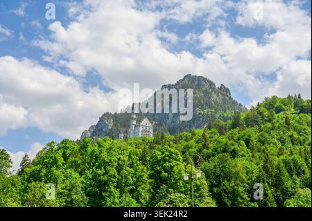Schwangau, Germania - maggio 31 2026: Vista distante del castello di Neuschwanstein, annidato su un aspro pendio di montagna circondato da verdi foreste sotto una nuvolosa Foto Stock