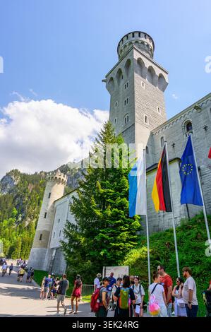 Schwangau, Germania - maggio 31 2026: I turisti si radunano vicino all'ingresso del castello di Neuschwanstein con bandiere nazionali che sventolano di fronte alle torreggianti S. Foto Stock