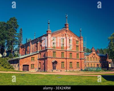 Kouvola, Finlandia - 16.08.2020: Grande fabbrica di mattoni d'epoca caratterizzata da torrette ornate e cornici gialle per finestre in mezzo al verde paesaggio Foto Stock