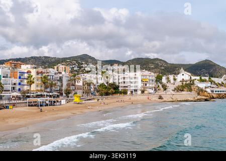 Spiaggia di Sitges e passeggiata costiera con la chiesa di Sant Bartomeu a Sitges, Spagna Foto Stock