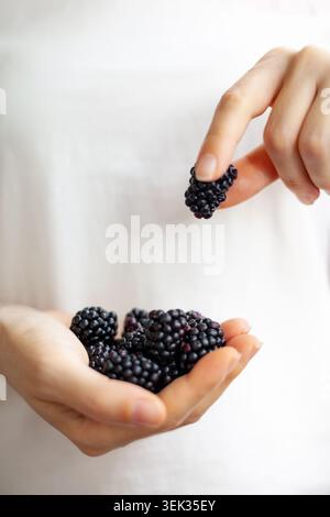 Foto verticale di una giovane donna che tiene in mano una manciata di more crude appena raccolte. Alimentazione sana, cibo biologico e concetto di raccolto estivo. Selecti Foto Stock