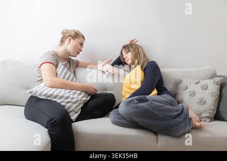 Due donne si sono impegnate a conversare su un divano grigio chiaro, una con un cuscino a righe e l'altra con un cuscino decorativo giallo, in un accogliente interno Foto Stock