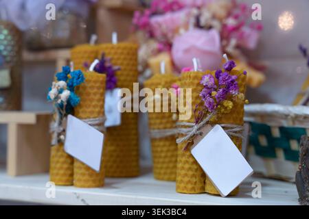 Candele di cera d'api naturali decorate con fiori secchi e etichette vuote su uno scaffale dell'officina Foto Stock