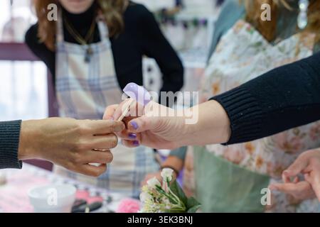 Mani che realizzano e passano una piccola decorazione a cera viola durante un laboratorio creativo Foto Stock