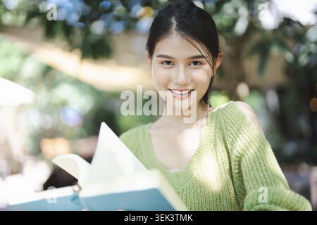 Bella donna asiatica che legge libri, studia o studia nel campus, ritratti, felicità all'aperto nel parco universitario Foto Stock