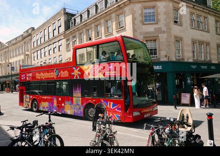 Autobus a due piani Red City Sightseeing in una strada di Bath, Somerset, Regno Unito, con edifici storici georgiani e biciclette parcheggiate Foto Stock