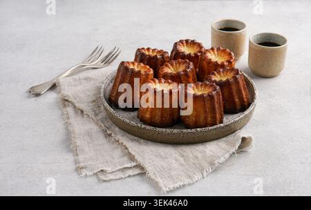 Vista ravvicinata del tradizionale dessert francese Canneles de Bordeaux. Gruppo di torte dolci alla vaniglia con crosta croccante caramellata su piatto di ceramica, se Foto Stock