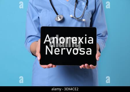 Medico in possesso di un biglietto con le parole anoressia nervosa su sfondo blu, primo piano Foto Stock