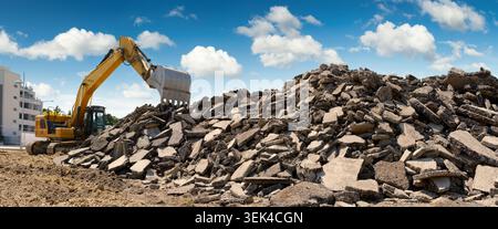 Un escavatore giallo che accumula macerie in un cantiere, con un bel cielo blu, vista panoramica Foto Stock
