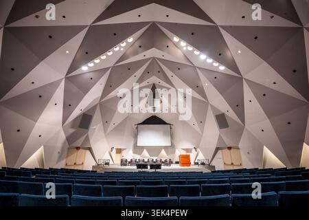 Vista posteriore dell'Auditorium Fred Kavli della National Academy of Sciences a Washington DC | WASHINGTON D.C., Stati Uniti — L'Auditorium Fred Kavli dell'edificio della National Academy of Sciences, visto dalla parte posteriore dell'edificio, rivela un soffitto composto da facce triangolari angolari interconnesse che avvolgono la sala dal muro posteriore al palco. L'auditorium è stato inaugurato nel 1970, offrendo all'Accademia la sua prima sala costruita appositamente per grandi pubblico e liberando la Grande Sala dorata del 1924 — con il programma del cupolo allegorico di Hildreth Meière — dal servizio di sala riunioni quotidiana. Foto Stock
