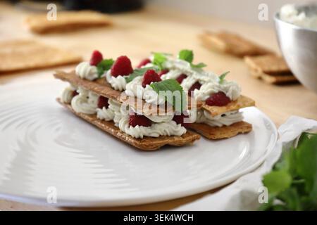 Dolce tradizionale francese mille feuille con lamponi freschi, panna montata e foglie di menta servito su un piatto bianco. Servizio di pasticceria per buongustai Foto Stock