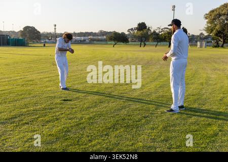 Due giocatori di cricket adulti in divisa bianca in piedi su un campo erboso che tiene una palla da cricket vicino alle reti Foto Stock