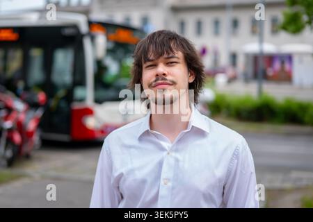 Giovane uomo in camicia bianca in piedi vicino al City bus durante l'estate in Austria Foto Stock