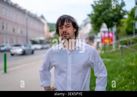 Ritratto di un giovane uomo con barba e capelli lunghi sullo sfondo della città Foto Stock
