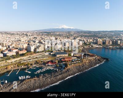 Veduta aerea del Deposito Locomotive di Catania lungo la costa rocciosa con il vulcano Etna innevato sullo sfondo a Catania, in Sicilia, Foto Stock