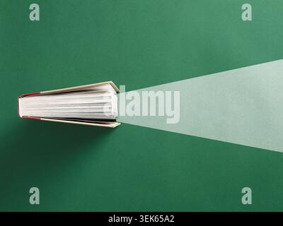 Libro aperto su sfondo verde che proietta un fascio di luce, che rappresenta l'istruzione, l'apprendimento, l'alfabetizzazione e l'illuminazione intellettuale. Foto Stock