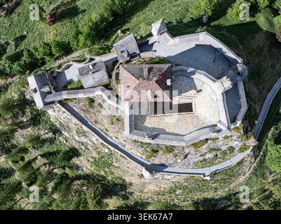 Vista aerea del castello di Tarasp con fortificazioni in pietra, tetti piastrellati e mura difensive circondate da una lussureggiante foresta verde a Scuol, Graubunden Foto Stock
