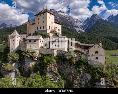 Vista aerea dello Schloss Tarasp, un castello medievale arroccato su una collina rocciosa circondata da lussureggianti foreste e dalle Alpi svizzere sotto un cielo spettacolare a Scuol, Foto Stock