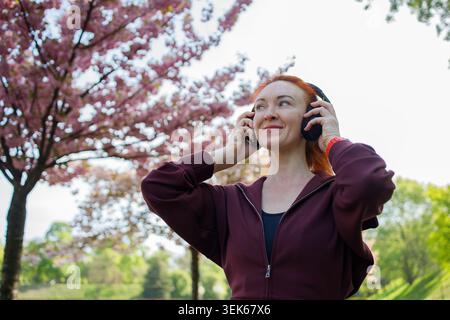 Zenzero donna di mezza età con grandi cuffie che si divertono ad ascoltare il Foto Stock